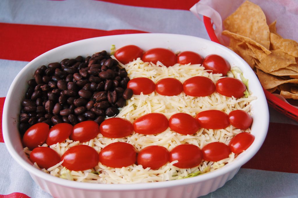 7 layer flag dip in a white casserole dish with chips