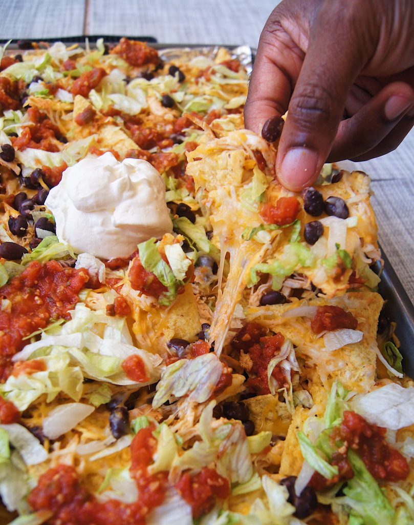 Sheet-Pan-Chicken-Nachos-with-hand-holding-a-chip